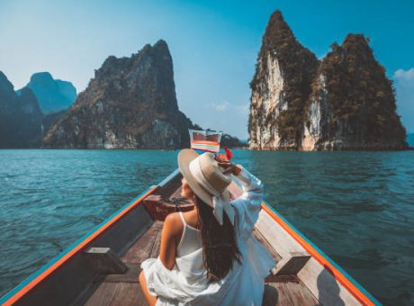 Travel summer vacation concept, Happy solo traveler asian woman with hat relax and sightseeing on Thai longtail boat in Ratchaprapha Dam at Khao Sok National Park, Surat Thani Province, Thailand